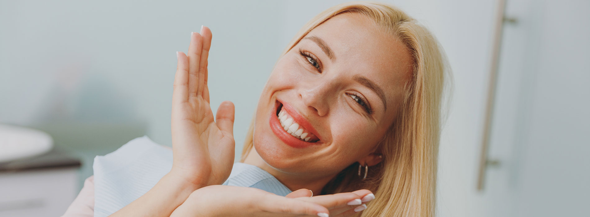 A woman with blonde hair smiling broadly at the camera while holding her hands outward.