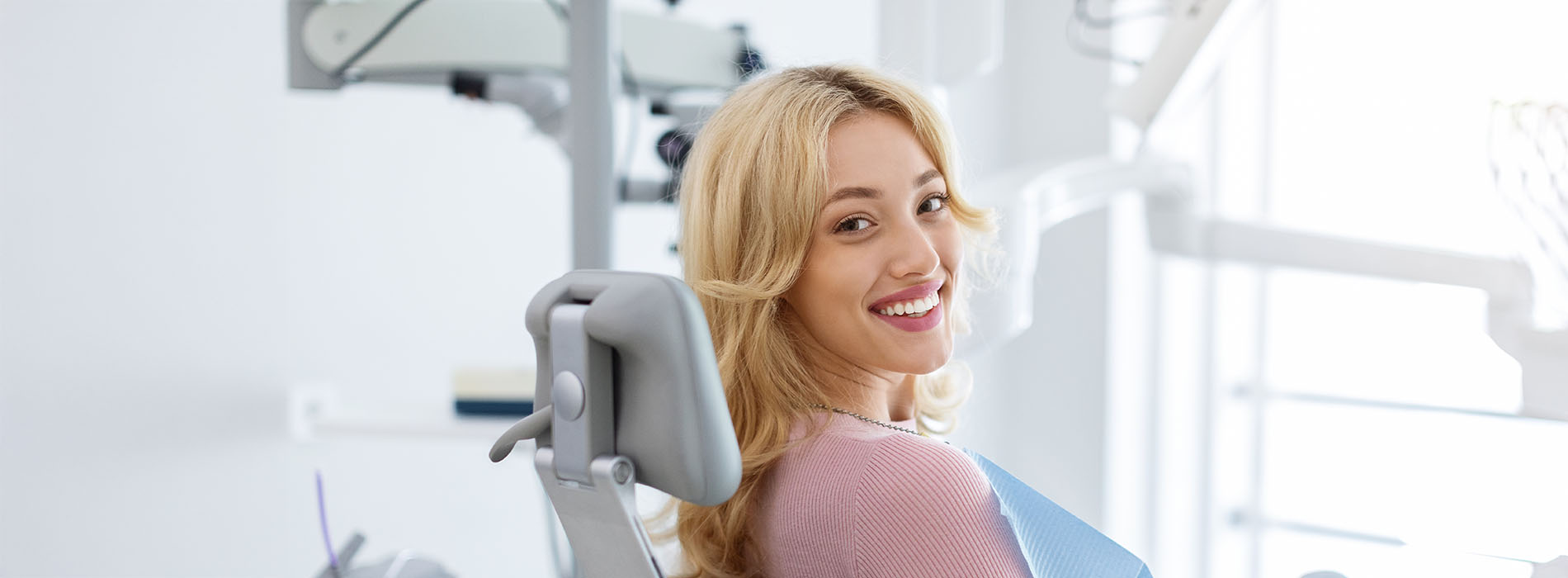 Woman sitting on dental chair with bright smile, looking directly at camera.