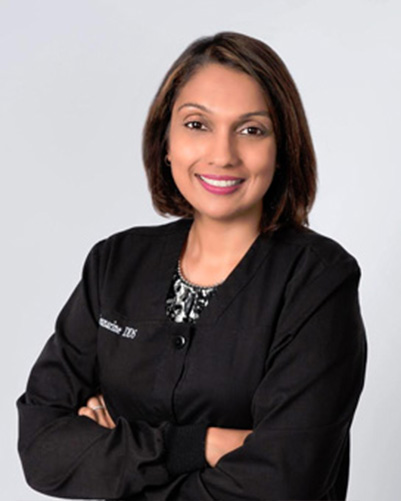 A woman with short hair wearing a black jacket and a name tag, standing against a white background.
