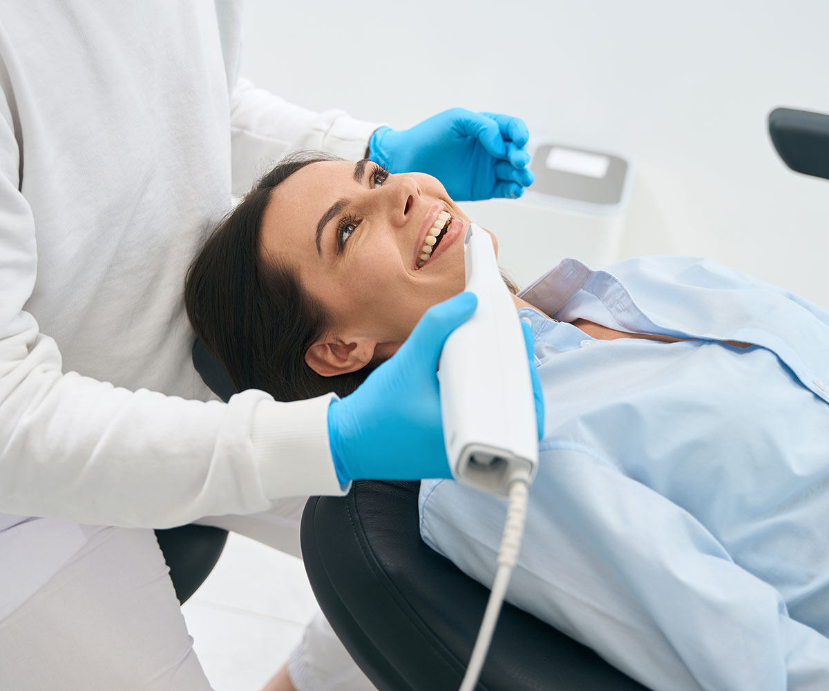 A woman receiving dental treatment, with a dental hygienist using an electric device on her teeth.